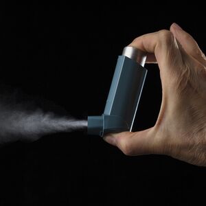 Close up view of blue asthma inhaler with spray coming out. Black background
