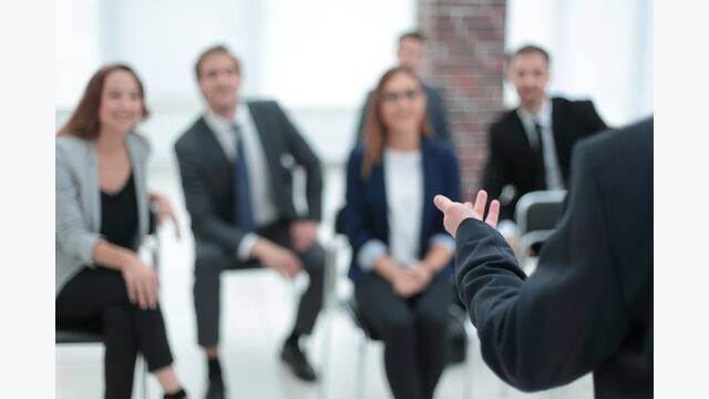 Der Coach in einem Seminar bringt einem Raum voller Geschäftsleute Kursinhalte näher.
