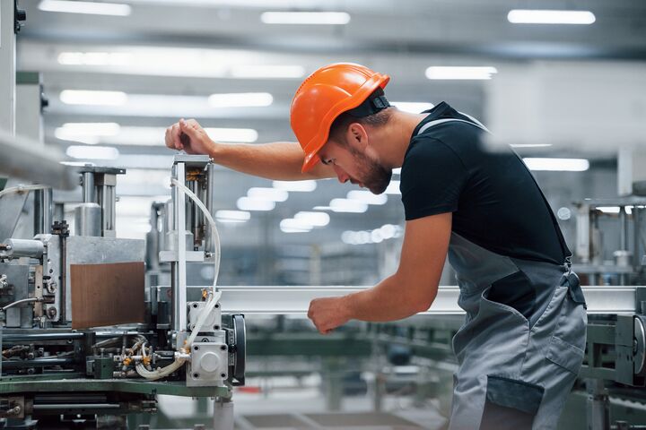 Operator of machine. Industrial worker indoors in factory. Young technician with orange hard hat.