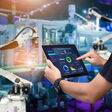 Hands holding tablet on blurred automation machine as background