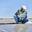 Mann mit Helm und Notebook vor Solarpaneelen