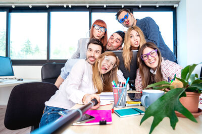 © Getty Images Young people employee workers taking happy selfie with stick - Life style concept of human resource on working fun time - Startupper at college office - Bright azure filter
