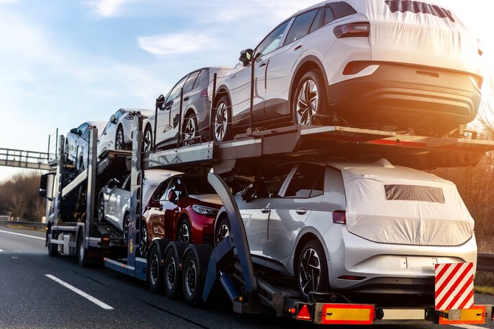 Tow truck car carrier semi trailer on highway carrying batch of new wrapped electric SUVs on motorway road at sunset evening time. Business distribution logistics service. Lorry driving highway.