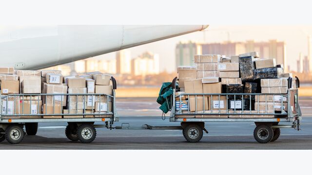 Close-up detail view of cargo cart trolley full with commercial parcels against turboprop cargo plane. Air mail shipping and logistics. Import export operations. Commercial charter flight service.