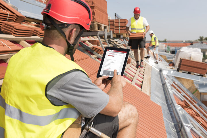 Zwei Arbeiter in gelben Schutzwesten und Helm auf Ziegeldach