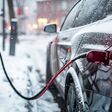 An electric car is parked at a charging station in the snow. This image can be used to illustrate eco-friendly transportation and the use of electric vehicles in winter conditions