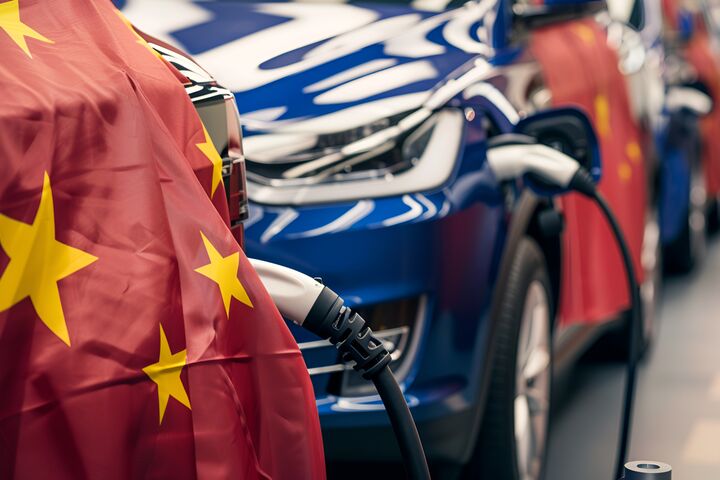 A line of electric cars are being charged at an event, with a Chinese flag in the foreground. The automotive design, wheels, and electric blue colors stand out
