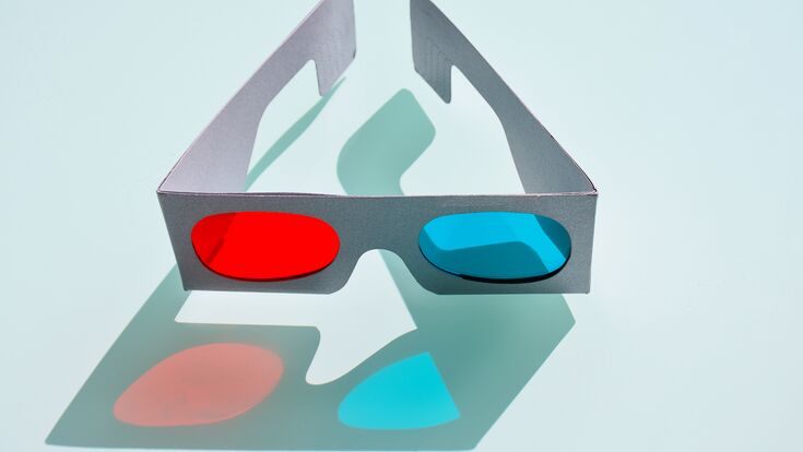 close up of a fun 3d glasses made with cardboard and plastic to create cheap tree optical perception by eyes seeing films at cinema.The glasses have two lens in red and blue colors on blue background