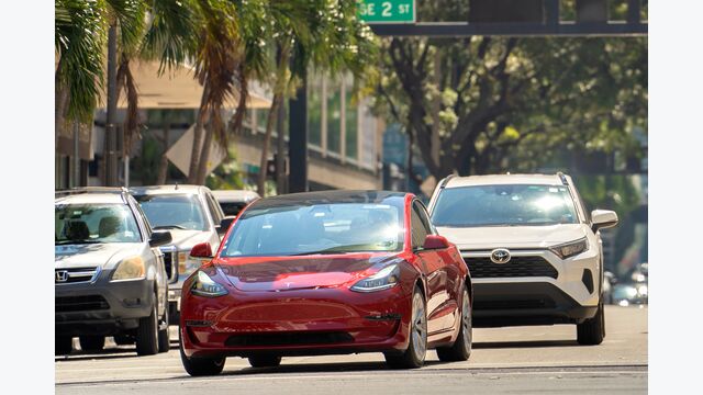 Tesla electric vehicle driving at intersection on American street with traffic lights in Miami, Florida. USA transportation. Miami, USA - March 1, 2023.