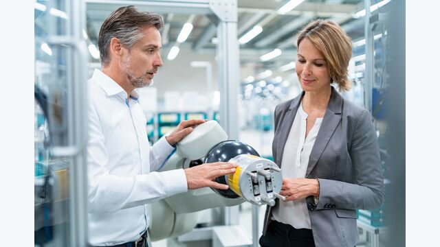 Businesswoman and man talking at assembly robot in a factory
