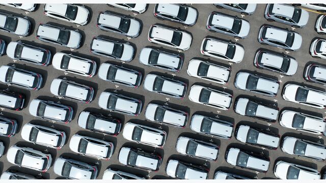 Aerial view of new cars stock at factory parking lot. Above view cars parked in a row. Automotive industry. Logistics business. Import or export new cars at warehouse. Big parking lot at port terminal