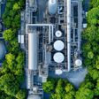 Aerial view of an industrial facility surrounded by lush green trees, showcasing blend of nature and industry. image captures intricate network of pipes and storage tanks.