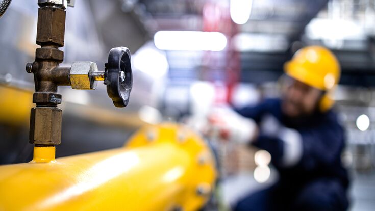 Close up view of natural gas pipeline with valve and refinery worker working in the background.