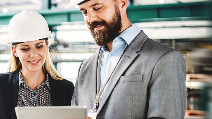 Eine Frau und ein Mann mit weißem Bauhelm, die sich etwas auf einem Tablet ansehen