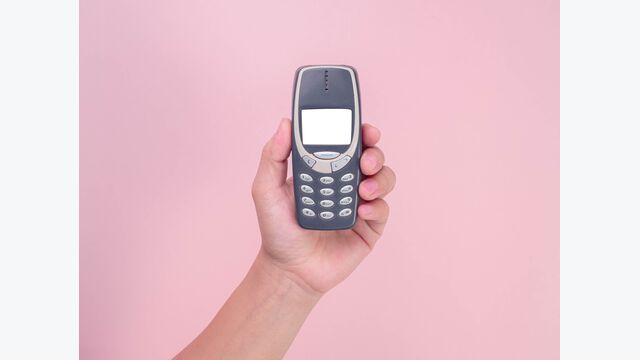 Close up hand holding mobile phone Nokia 3310 isolated on pink background. Female hand holding old used phone Nokia 3310.