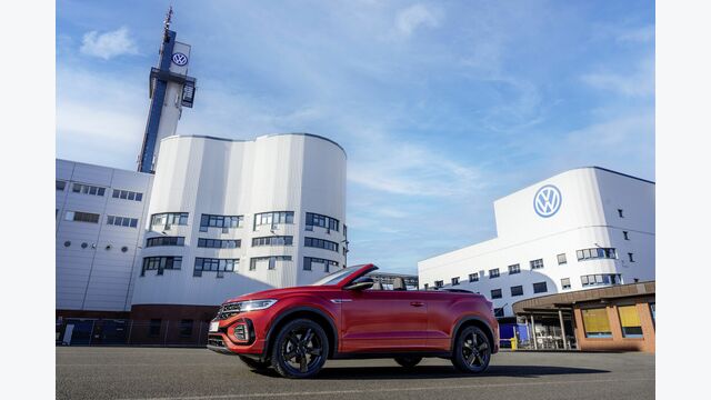 Rotes Volkswagen-Cabrio vor dem VW-Werk Osnabrück mit sichtbarem Volkswagen-Logo am Gebäude.