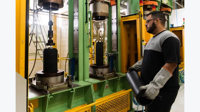 Continental-Mitarbeiter bedient Maschinen in der Reifenproduktion und hält ein schwarzes Gummiteil in den Händen.