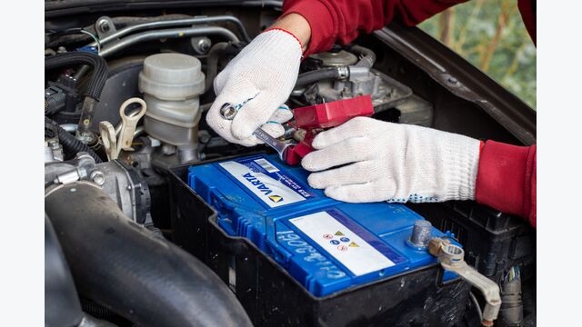 Ein Mann schraubt die Anschlüsse einer Varta-Autobatterie unter der Motorhaube eines Fahrzeugs fest.