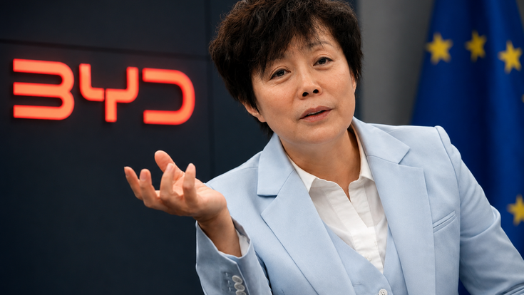 BYD-Managerin vor BYD-Logo und EU-Flagge bei einem Gespräch über die Europa-Strategie des chinesischen Elektroautobauers.