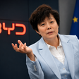 BYD-Managerin vor BYD-Logo und EU-Flagge bei einem Gespräch über die Europa-Strategie des chinesischen Elektroautobauers.