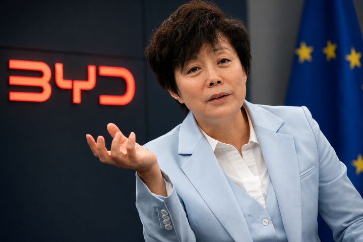 BYD-Managerin vor BYD-Logo und EU-Flagge bei einem Gespräch über die Europa-Strategie des chinesischen Elektroautobauers.