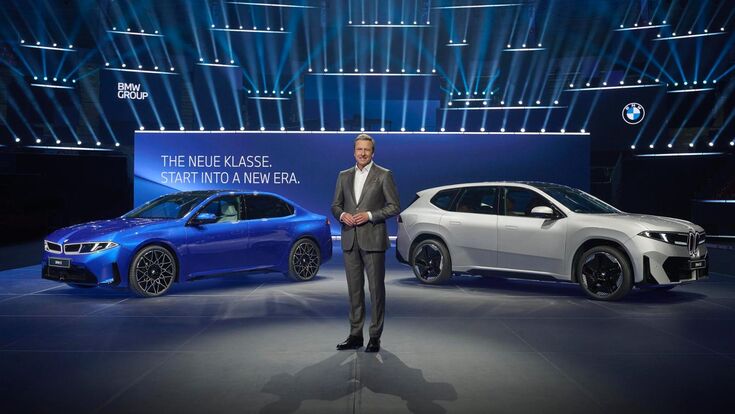 BMW präsentiert die Neue Klasse auf einer Bühne mit zwei Elektroautos, darunter ein weißer BMW iX3, vor großem Schriftzug „The Neue Klasse. Start into a new era“.