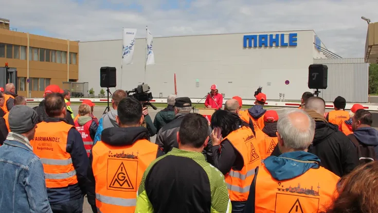 Beschäftigte mit IG-Metall-Westen vor einem Mahle-Werk mit sichtbarem Firmenlogo.