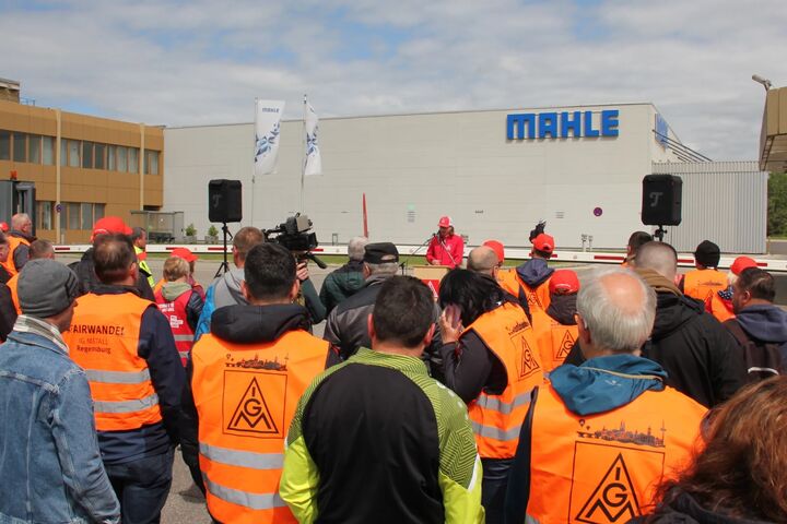 Beschäftigte mit IG-Metall-Westen vor einem Mahle-Werk mit sichtbarem Firmenlogo.