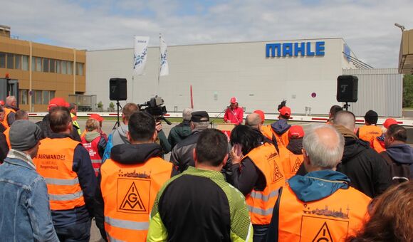 Beschäftigte mit IG-Metall-Westen vor einem Mahle-Werk mit sichtbarem Firmenlogo.