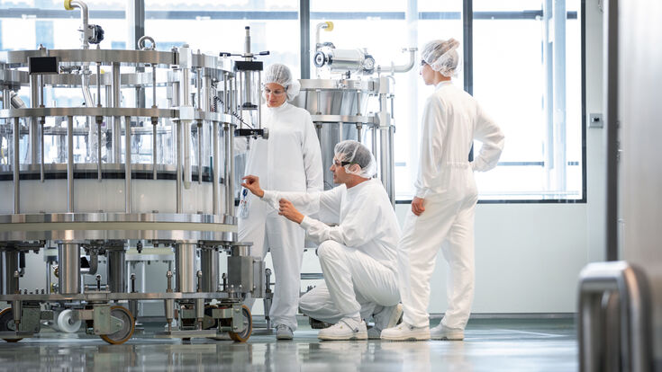 Drei Beschäftigte in Schutzkleidung kontrollieren eine Anlage in einer sterilen Pharmaproduktion.