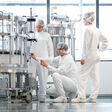 Drei Beschäftigte in Schutzkleidung kontrollieren eine Anlage in einer sterilen Pharmaproduktion.