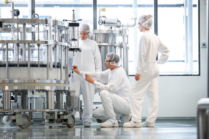 Drei Beschäftigte in Schutzkleidung kontrollieren eine Anlage in einer sterilen Pharmaproduktion.