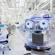Reinraum in einer Chipfabrik mit technischer Anlage im Vordergrund und einer Person in Schutzkleidung an einem Arbeitsplatz.