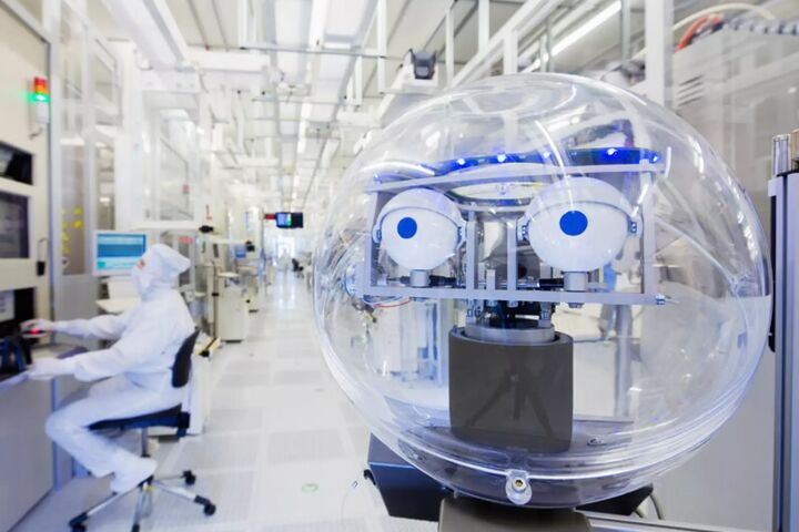 Reinraum in einer Chipfabrik mit technischer Anlage im Vordergrund und einer Person in Schutzkleidung an einem Arbeitsplatz.