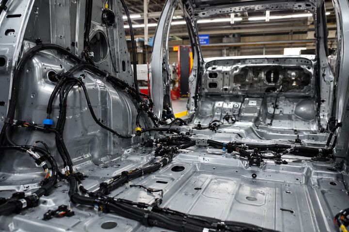 Innenansicht einer Rohkarosse in einer Autofabrik. Mehrere schwarze Kabelbäume und Bordnetzleitungen sind entlang des Fahrzeugbodens und der Seitenwände verlegt.
