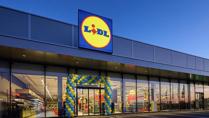 Lidl-Filiale mit beleuchtetem Lidl-Logo und Eingang im Abendlicht.