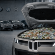Ein grauer BMW steht in einer Werkstatt mit geöffneter Motorhaube, darunter liegen viele Euro-Scheine. Im Hintergrund sind unscharf die Logos von BMW, Volkswagen und Mercedes zu sehen.
