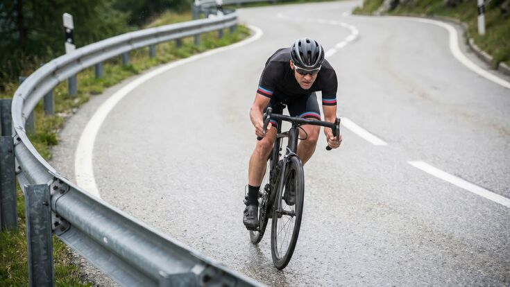Road cyclist descending sharp mountain curve in performance gear speed endurance training racing concept on winding alpine asphalt with focus determination motion or fitness challenge