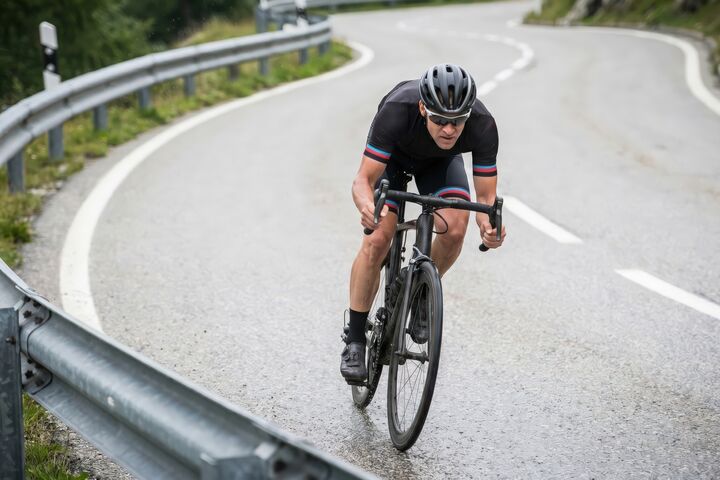 Road cyclist descending sharp mountain curve in performance gear speed endurance training racing concept on winding alpine asphalt with focus determination motion or fitness challenge