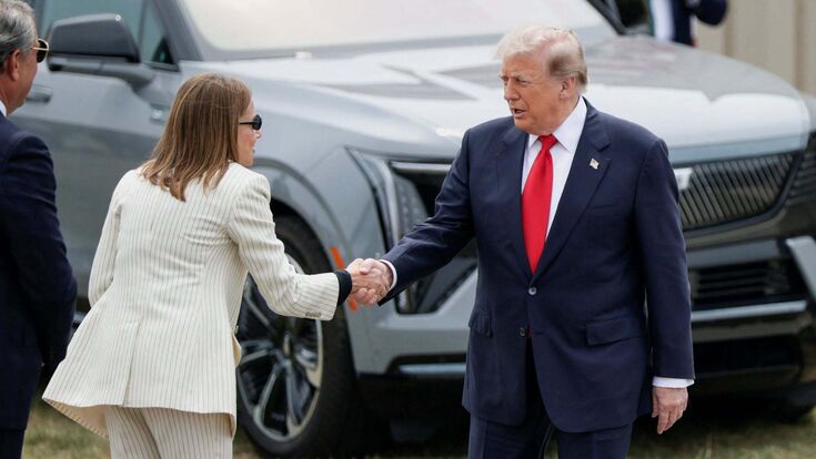 Donald Trump und General-Motors-Chefin Mary Barra bei einem Auftritt in Michigan vor US-Flaggen und GM-Fahrzeugen.