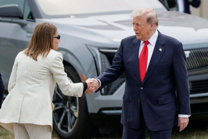 Donald Trump und General-Motors-Chefin Mary Barra bei einem Auftritt in Michigan vor US-Flaggen und GM-Fahrzeugen.