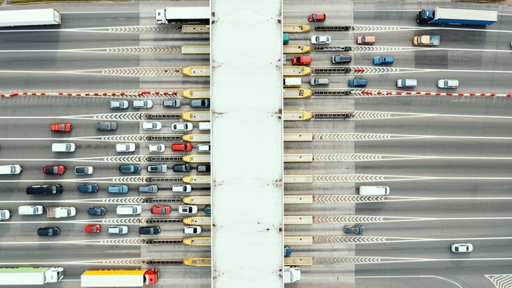 An overhead view of a busy toll road with many cars queuing up to pay the highway toll