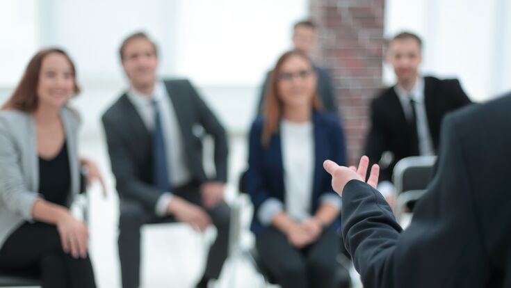 Der Coach in einem Seminar bringt einem Raum voller Geschäftsleute Kursinhalte näher.