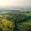 Luftansicht auf ein großes grünes Feld mit Wald und Windrädern.